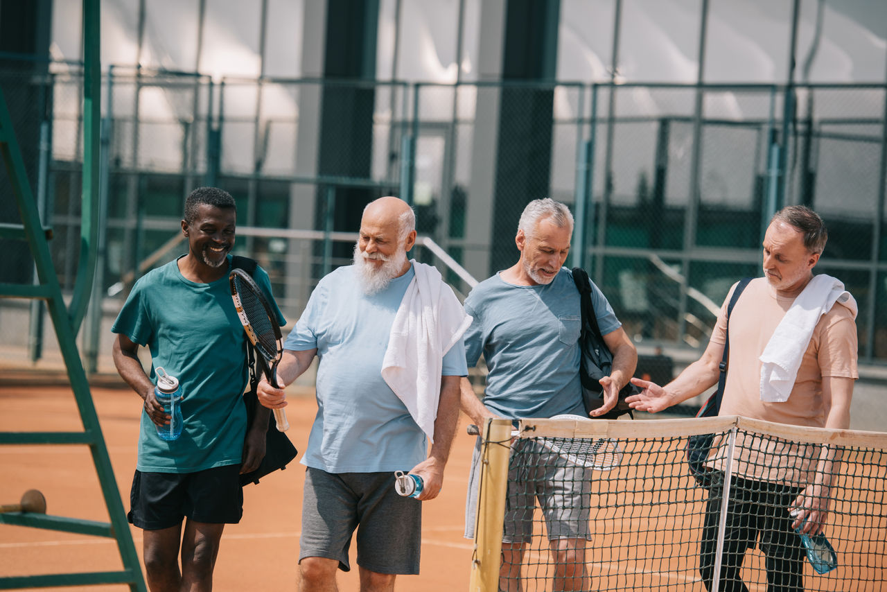 portrait of smiling multiracial elderly friends with tennis equipment on court