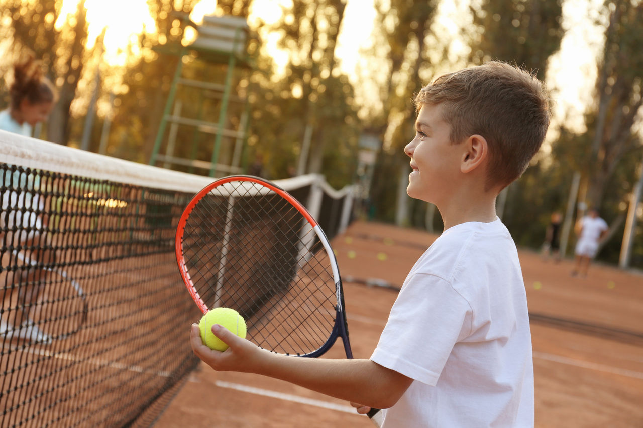 Cute little boy playing tennis on court outdoors