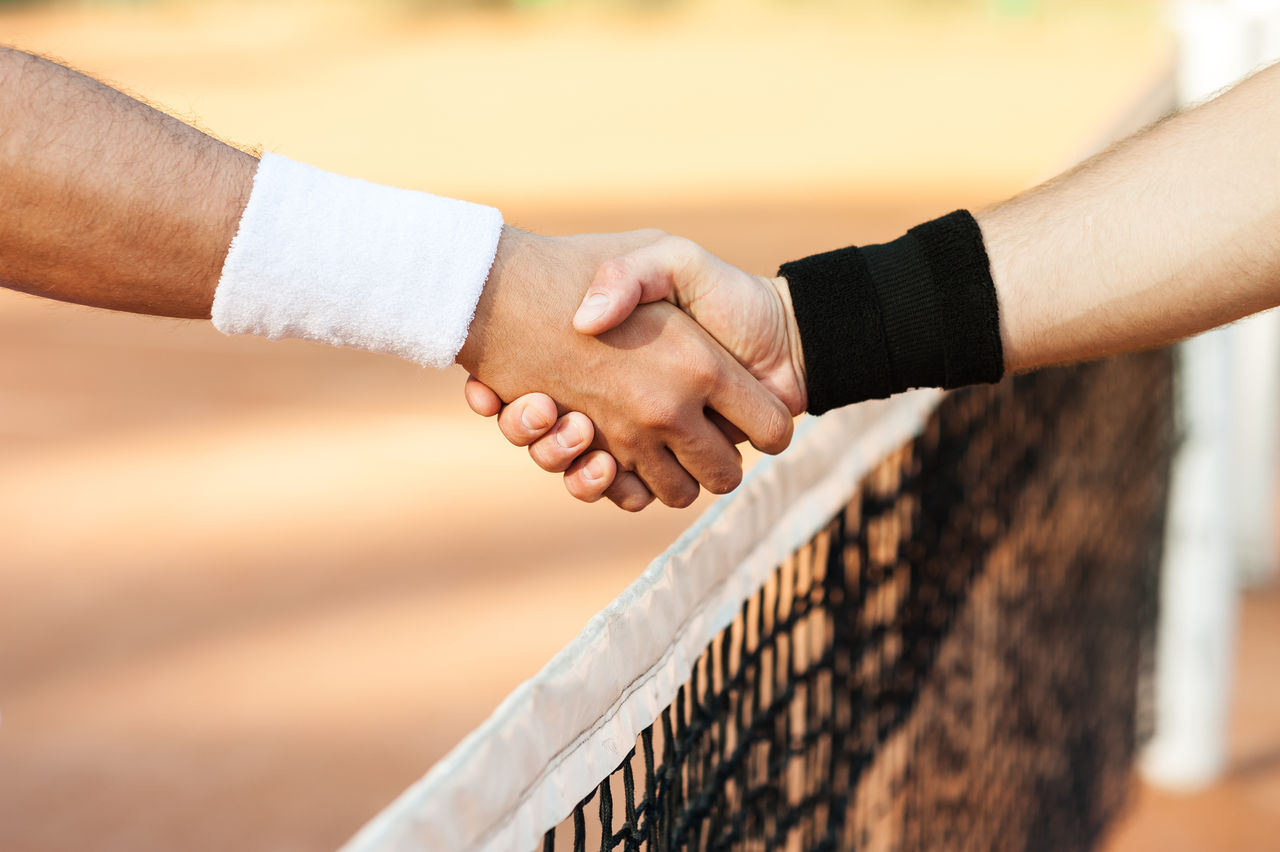 Close up photo of young men on tennis court. Men playing tennis. Men shaking hands above net before game