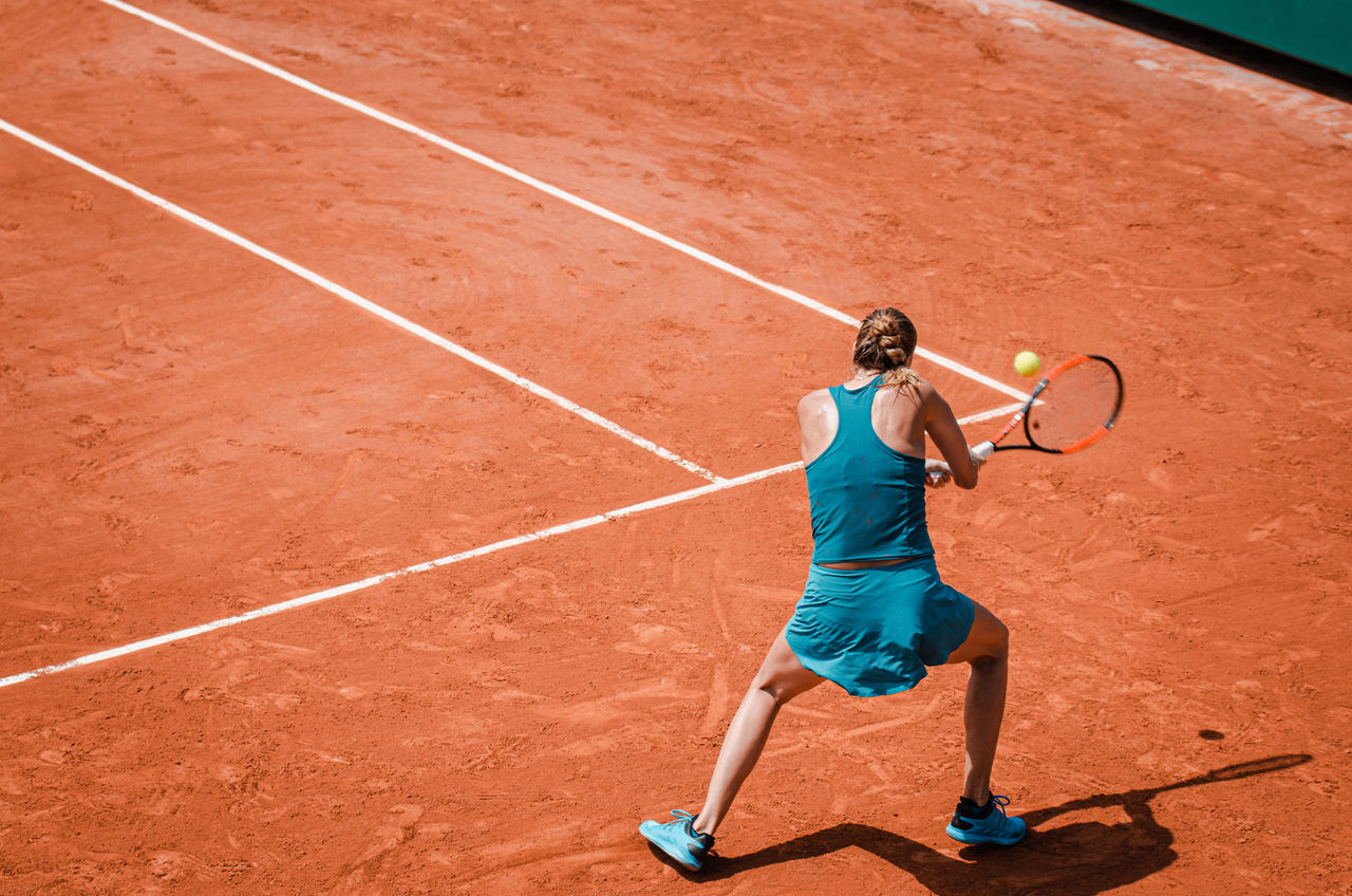 Back view  of a woman playing backhand in tennis outdoor competition game, running, professional