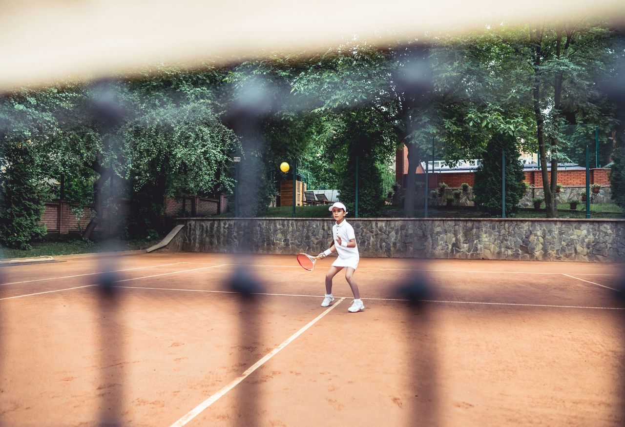 Full length shot of a sporty little girl on open tennis court. Child girl athlete playing tennis in the sport club. Active exercise for kids.