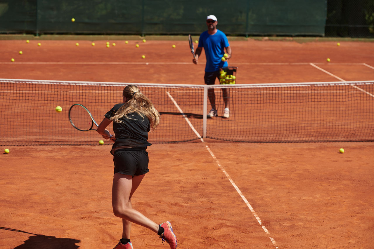 A professional tennis player and her coach training on a sunny day at the tennis court. Training and preparation of a professional tennis player.