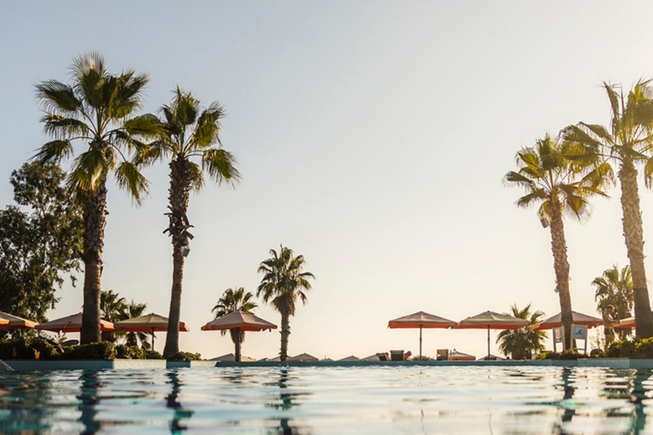 Pool mit Palmen und Sonnenschirmen am Horizont bei Sonnenuntergang