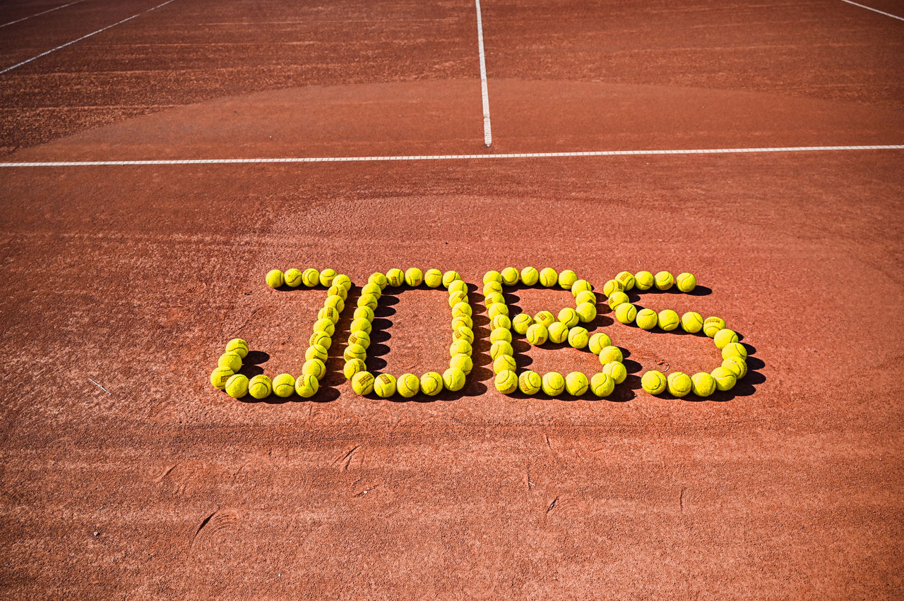 "Jobs"-Schriftzug mit Tennisbällen auf Tennisplatz