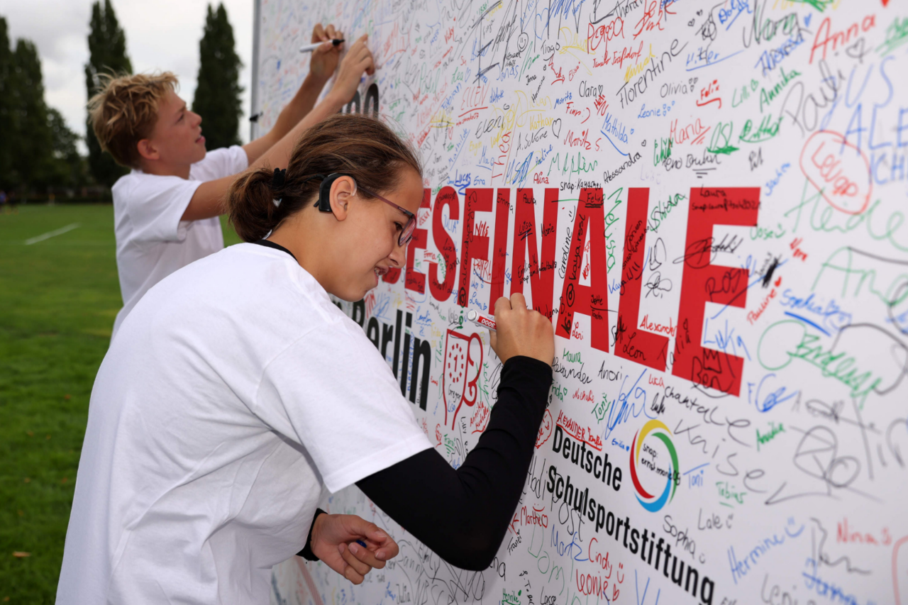 Kinder unterschreiben beim Bundesfinale an einer Wand