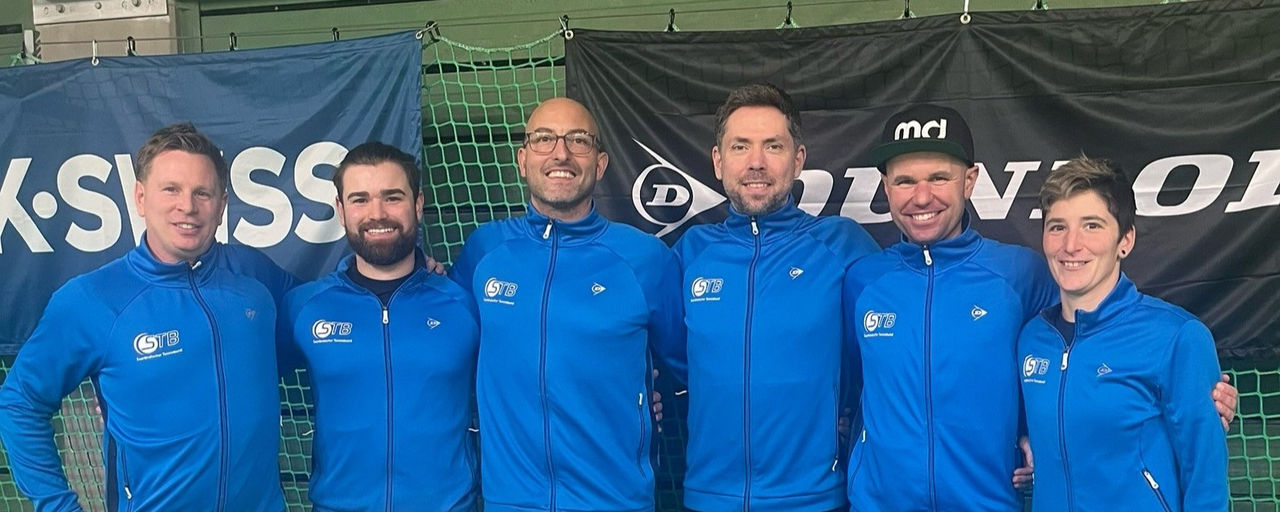 Trainerinnen und Trainer des STB nebeneinander Arm in Arm in der Tennishalle