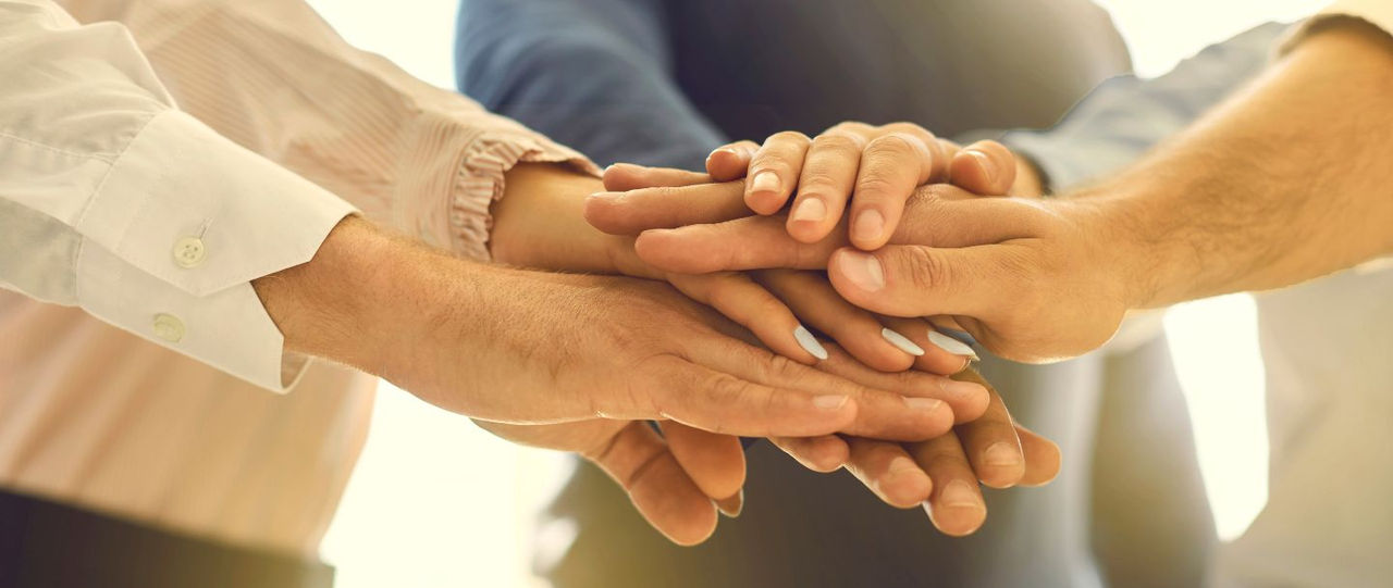 5 Hände, die aufeinanderliegen und Zusammenarbeit darstellen