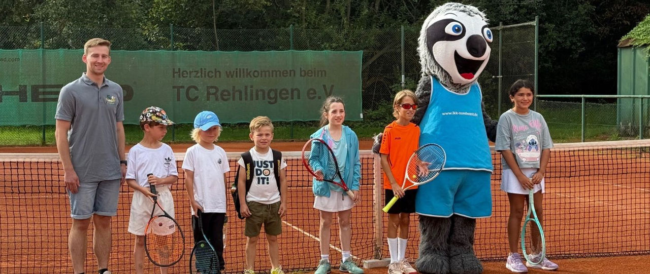 6 Kinder, ein Betreuer und das Maskottchen des STB Kis's Cup im Gruppenfoto mit Schlägern vor dem Netz