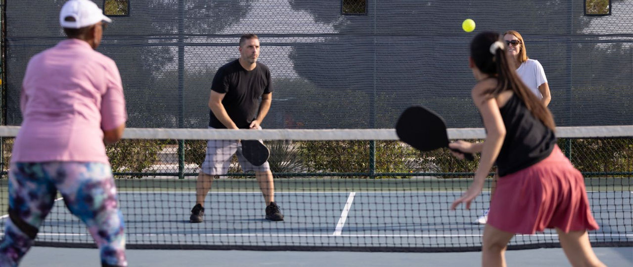 4 Personen stehen sich am Netz gegenüber und spielen Pickleball