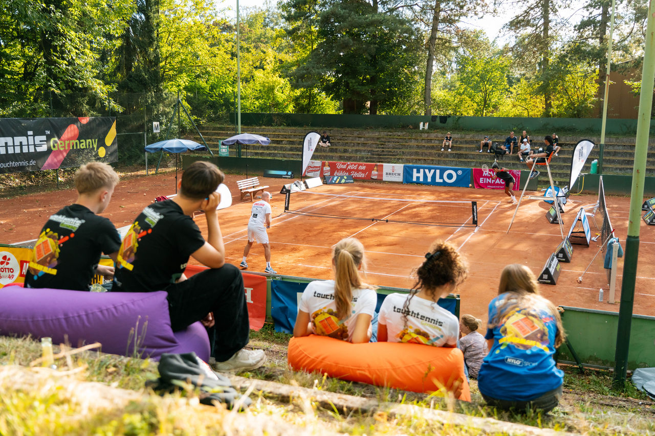 Zwei Spieler treten im touchtennis-Feld gegeneinander an - Zuschauer sitzen am Rand