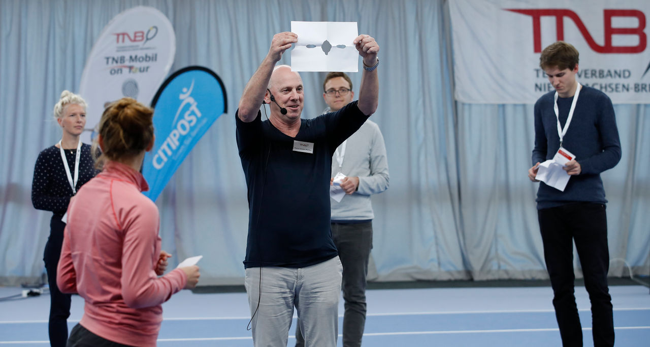 Trainer hält Zettel hoch und zeigt es den Schülern